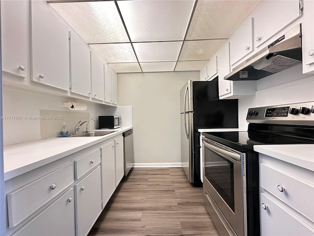 kitchen featuring white cabinets, a sink, light countertops, stainless steel appliances, and under cabinet range hood