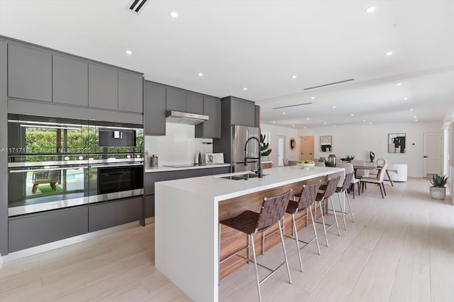 kitchen with under cabinet range hood, stainless steel appliances, a large island, modern cabinets, and a kitchen bar