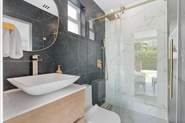 full bathroom featuring toilet, vanity, a marble finish shower, and tile walls