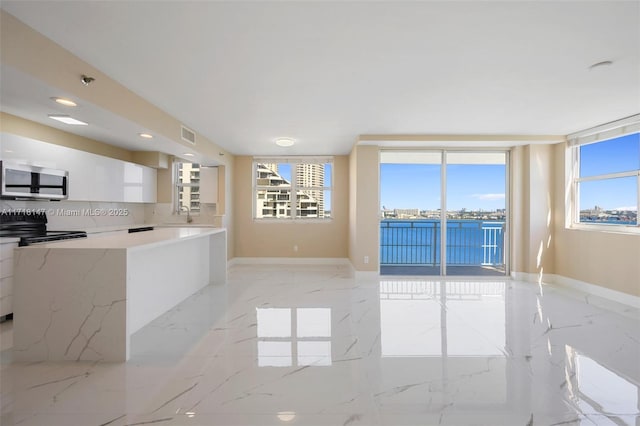 kitchen featuring backsplash, white cabinetry, stove, and a healthy amount of sunlight