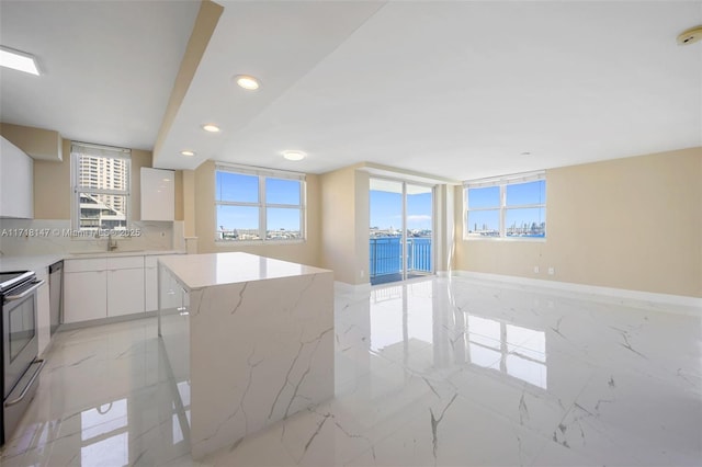 kitchen with decorative backsplash, a wealth of natural light, a kitchen island, range, and white cabinetry