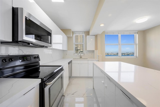 kitchen featuring white cabinetry, sink, light stone countertops, decorative backsplash, and appliances with stainless steel finishes