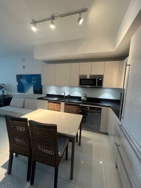 kitchen with light tile patterned floors, black oven, sink, and white cabinets