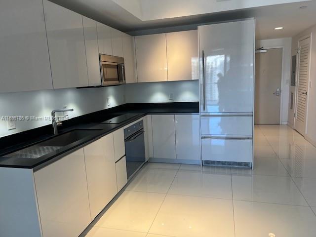 kitchen with sink, light tile patterned floors, white cabinets, and black appliances