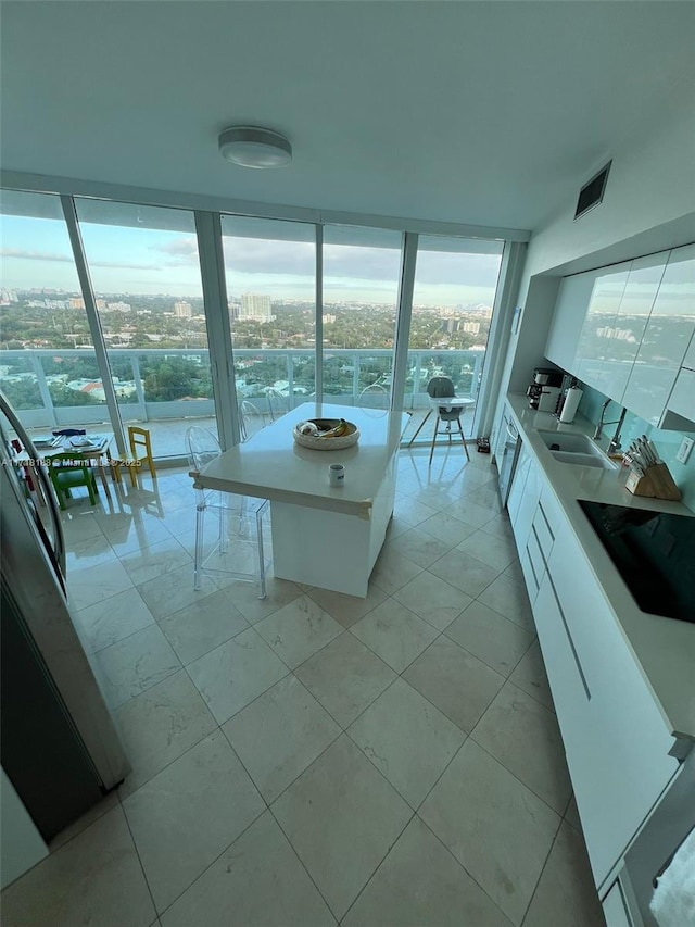 kitchen with floor to ceiling windows, sink, light tile patterned flooring, black electric cooktop, and white cabinets