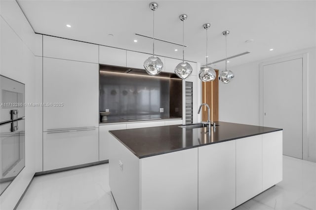 kitchen featuring decorative light fixtures, sink, white cabinetry, and an island with sink