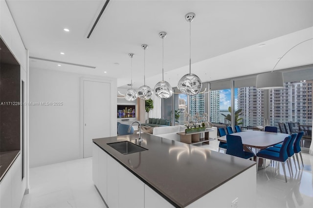 kitchen featuring floor to ceiling windows, a center island with sink, sink, decorative light fixtures, and white cabinetry