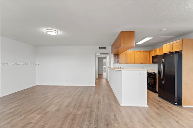 kitchen with light brown cabinets, kitchen peninsula, a textured ceiling, black appliances, and light wood-type flooring