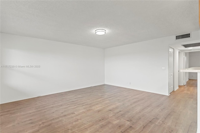 empty room with a textured ceiling and light hardwood / wood-style floors