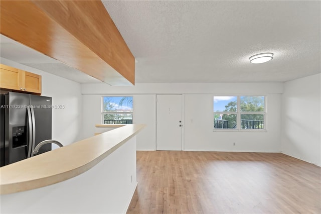 kitchen featuring stainless steel fridge, light brown cabinets, a textured ceiling, and light hardwood / wood-style flooring