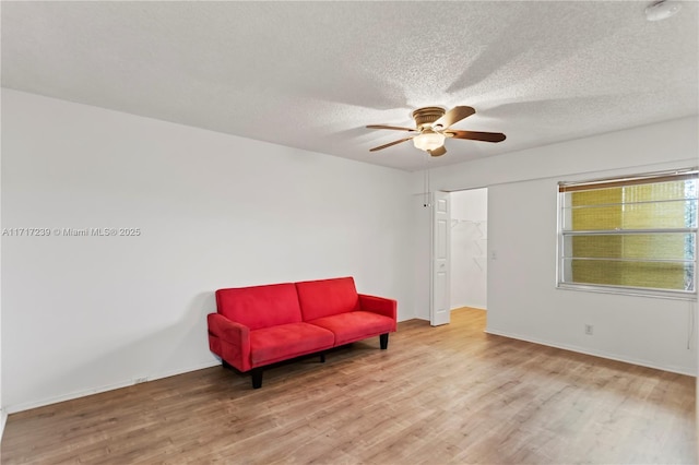 living area with ceiling fan, light hardwood / wood-style floors, and a textured ceiling