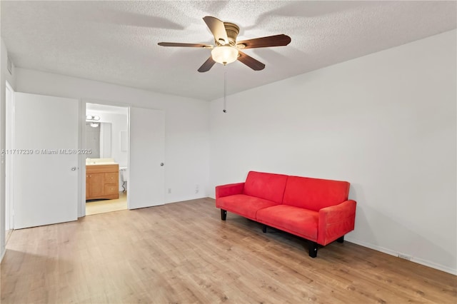 living area with ceiling fan, wood-type flooring, and a textured ceiling