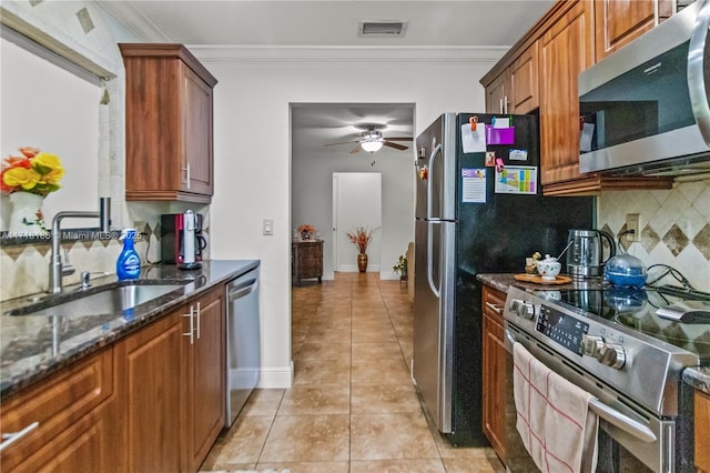 kitchen featuring appliances with stainless steel finishes, crown molding, sink, light tile patterned floors, and dark stone countertops