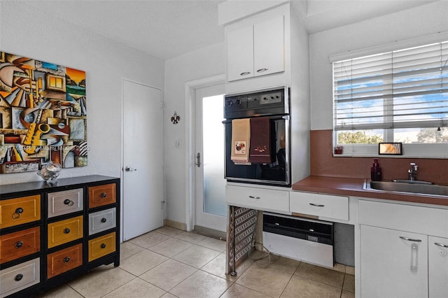 kitchen with white cabinets, light tile patterned flooring, oven, and sink