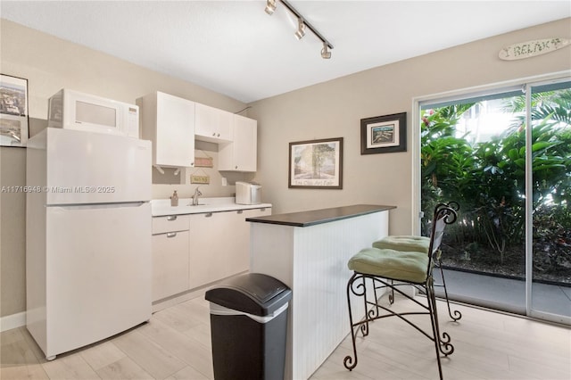 kitchen with white appliances, light hardwood / wood-style floors, white cabinetry, and a breakfast bar area