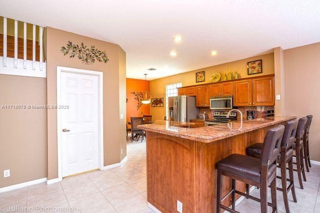 kitchen featuring kitchen peninsula, appliances with stainless steel finishes, tasteful backsplash, light tile patterned flooring, and light stone countertops