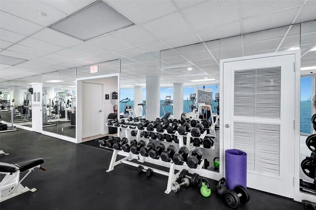 workout area featuring a paneled ceiling, a water view, and a healthy amount of sunlight