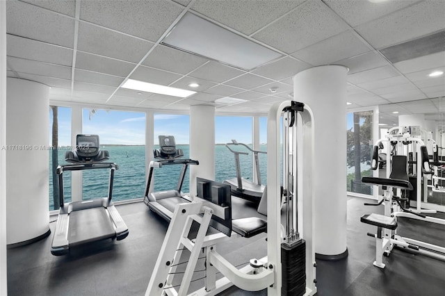 exercise room with a paneled ceiling, expansive windows, and a water view