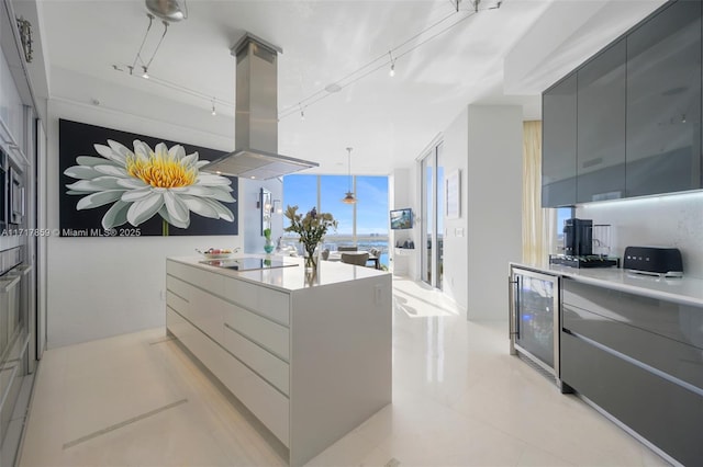 kitchen featuring island exhaust hood, black electric stovetop, rail lighting, pendant lighting, and wine cooler