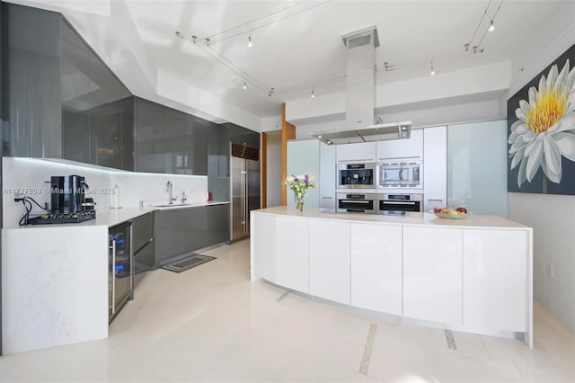 kitchen featuring built in appliances, island range hood, white cabinetry, and sink