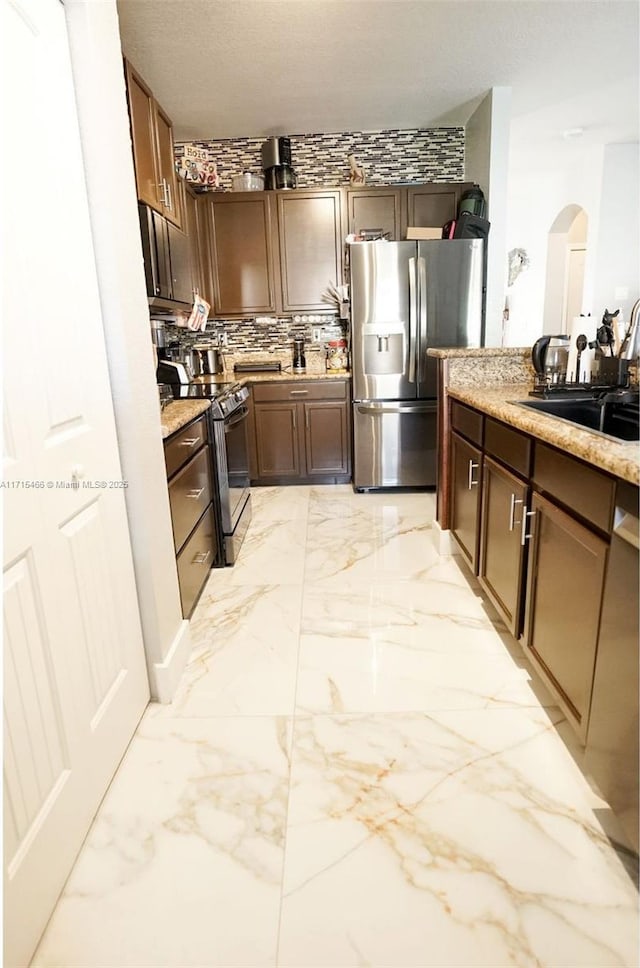 kitchen featuring sink, light stone counters, decorative backsplash, dark brown cabinets, and appliances with stainless steel finishes