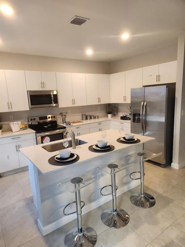 kitchen with a kitchen island with sink, white cabinets, a kitchen breakfast bar, sink, and appliances with stainless steel finishes