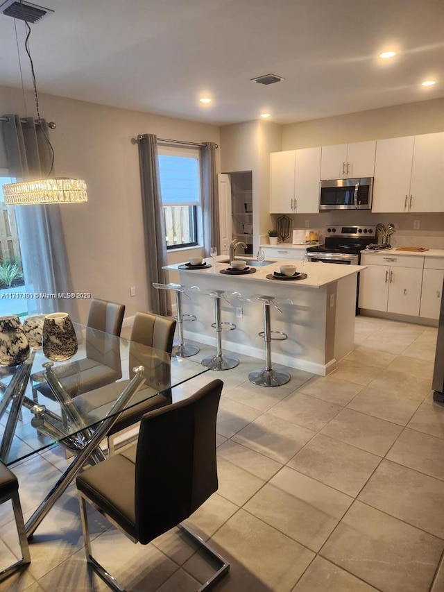 kitchen featuring a breakfast bar, stainless steel appliances, pendant lighting, white cabinetry, and an island with sink