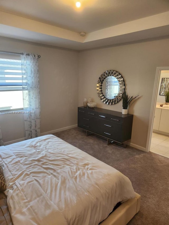 carpeted bedroom featuring ensuite bathroom and a tray ceiling