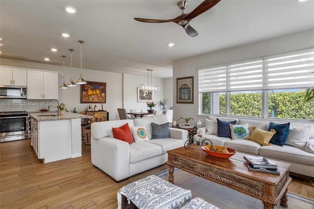 living room with sink, ceiling fan with notable chandelier, and light wood-type flooring