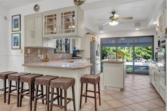 kitchen with stainless steel refrigerator with ice dispenser, light stone countertops, light tile patterned floors, tasteful backsplash, and white cabinetry