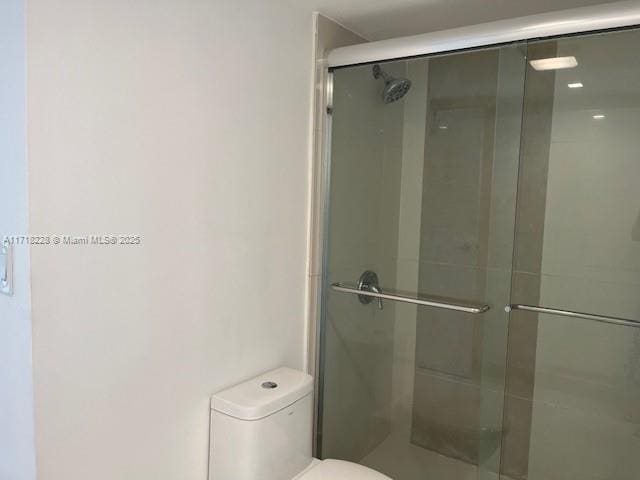 bathroom featuring a shower with shower door and toilet