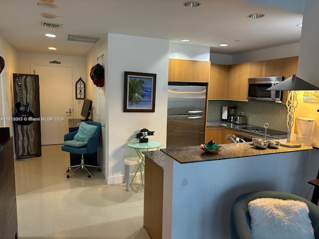 kitchen featuring appliances with stainless steel finishes, tasteful backsplash, light tile patterned flooring, kitchen peninsula, and dark stone counters