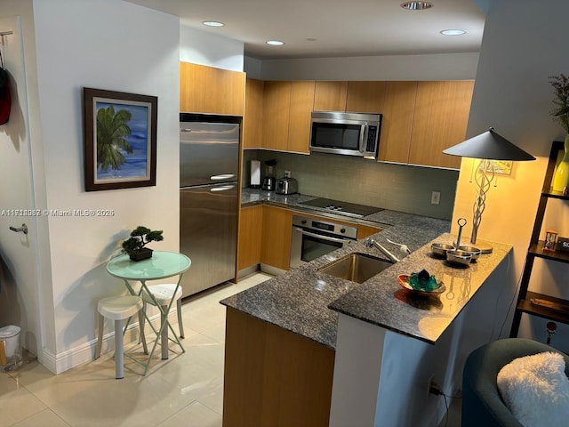 kitchen featuring sink, light tile patterned floors, stainless steel appliances, kitchen peninsula, and dark stone counters