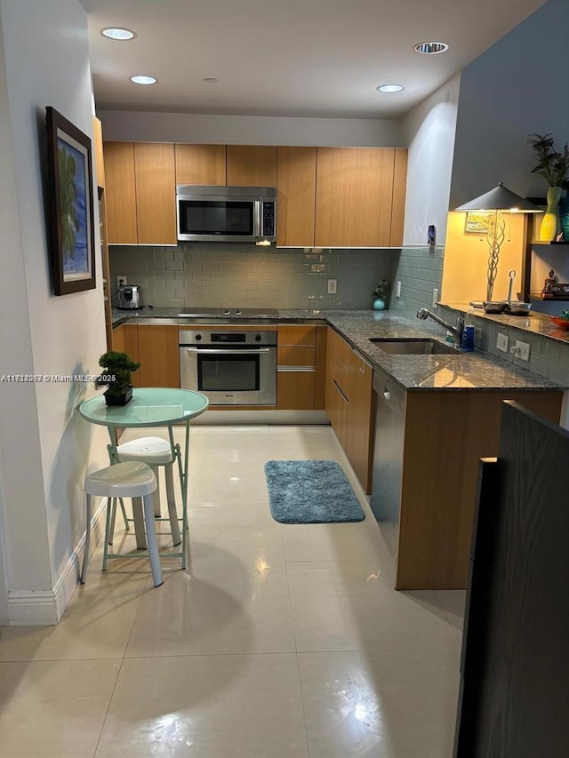 kitchen with tasteful backsplash, sink, dark stone counters, light tile patterned floors, and stainless steel appliances