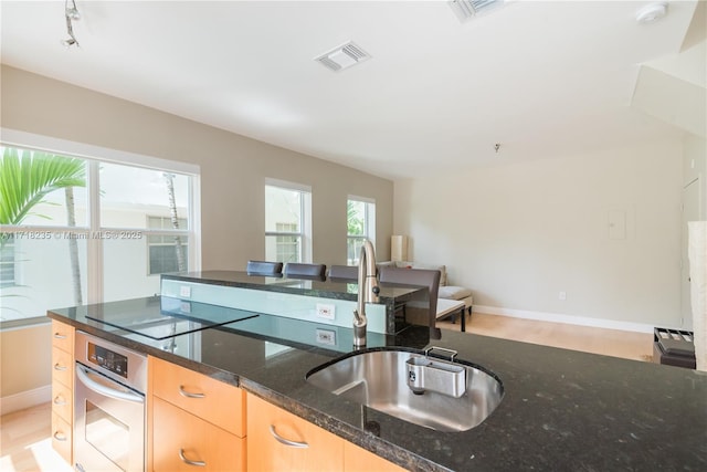 kitchen with light brown cabinets, dark stone counters, black electric stovetop, oven, and sink