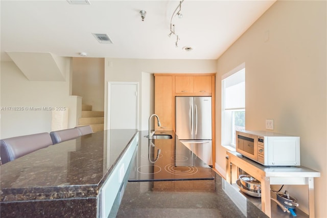 kitchen featuring stainless steel fridge, dark stone countertops, kitchen peninsula, and sink