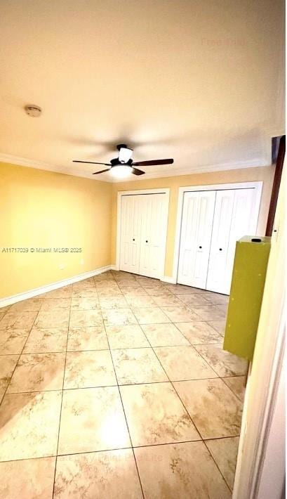 unfurnished bedroom with tile patterned floors, ceiling fan, crown molding, and multiple closets