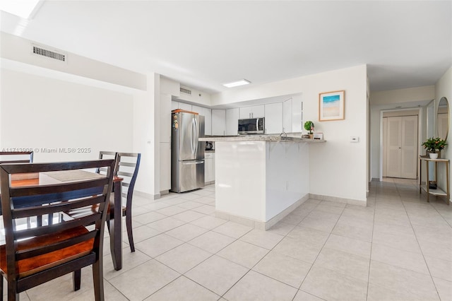 kitchen with white cabinetry, light tile patterned floors, kitchen peninsula, and appliances with stainless steel finishes