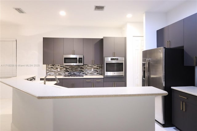 kitchen featuring gray cabinetry, sink, decorative backsplash, kitchen peninsula, and stainless steel appliances