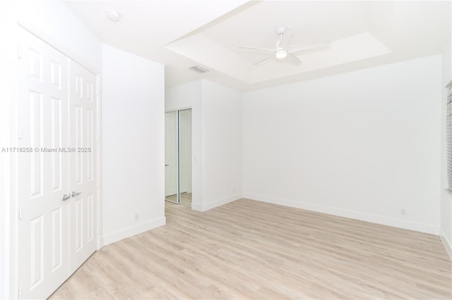 unfurnished room featuring ceiling fan, a raised ceiling, and light wood-type flooring