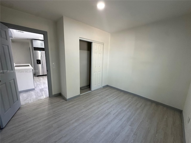 unfurnished bedroom with wood-type flooring, stainless steel refrigerator with ice dispenser, and a closet