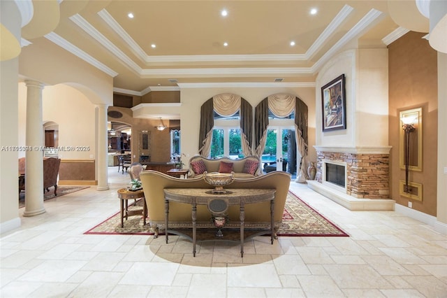 living area with ornate columns, a high ceiling, stone tile flooring, a stone fireplace, and a raised ceiling