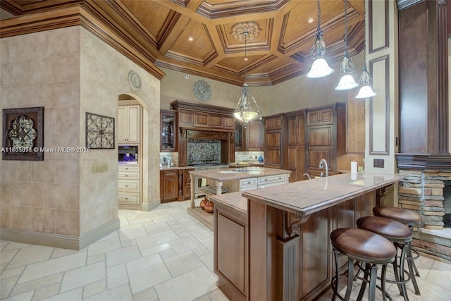 kitchen featuring stone tile floors, coffered ceiling, a high ceiling, light countertops, and crown molding