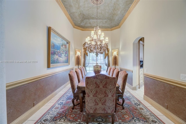 dining area with crown molding, a chandelier, light tile patterned floors, a towering ceiling, and arched walkways