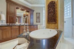 full bath featuring a textured ceiling, a jetted tub, vanity, and ornamental molding