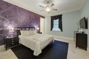 bedroom featuring an accent wall, a ceiling fan, baseboards, and ornamental molding