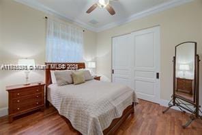 bedroom with wood finished floors, a closet, crown molding, baseboards, and ceiling fan