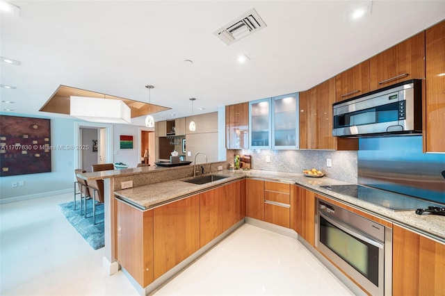 kitchen featuring sink, stainless steel appliances, light stone counters, kitchen peninsula, and pendant lighting