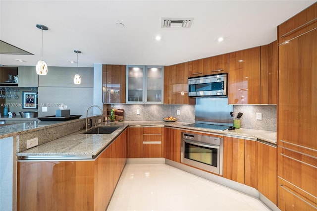 kitchen with kitchen peninsula, light stone counters, stainless steel appliances, sink, and decorative light fixtures