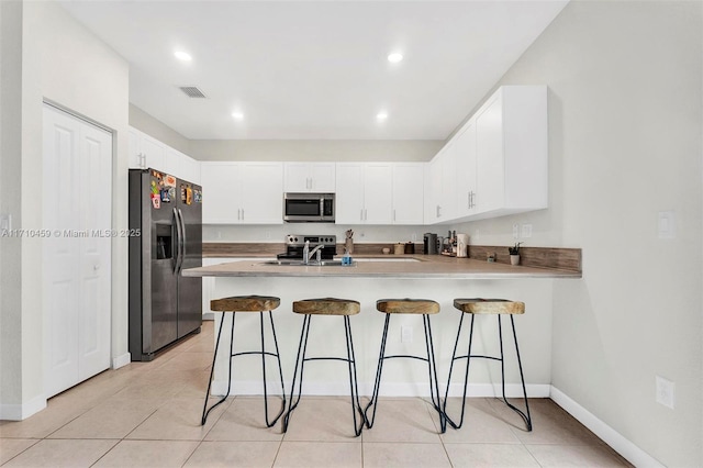 kitchen with a breakfast bar, white cabinets, light tile patterned floors, appliances with stainless steel finishes, and kitchen peninsula